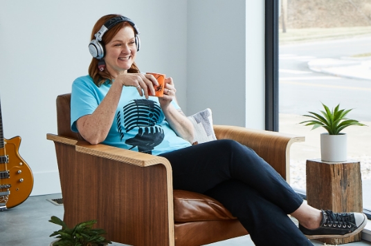 Rebecca relaxing in a chair while drinking coffee and listening to music on headphones