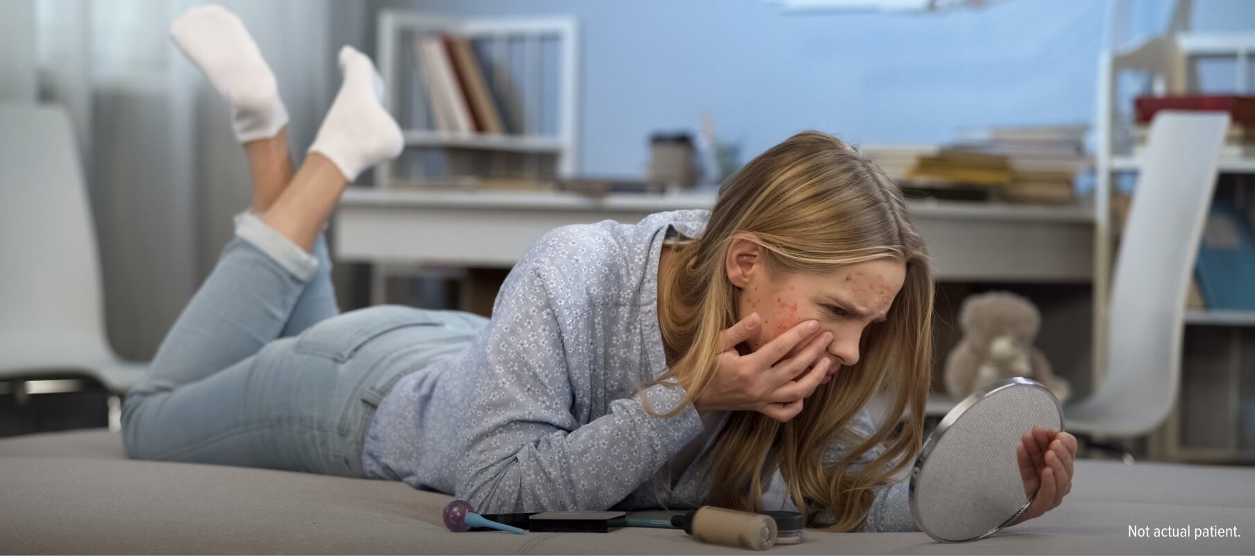 Young woman laying on her bed and touching her face while looking at herself in a small handheld mirror